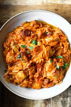 a white bowl filled with pasta and meat covered in sauce on top of a wooden table