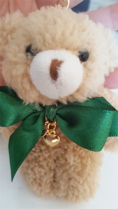 a brown teddy bear with a green bow on it's neck and a gold bell around its neck