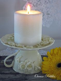 a white candle sitting on top of a cake plate with a yellow flower next to it