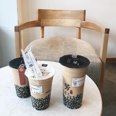 two cups of coffee sitting on top of a white table next to a wooden chair