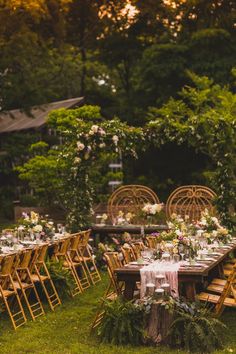 an outdoor dinner table set up with flowers and greenery on the tables, surrounded by wooden chairs