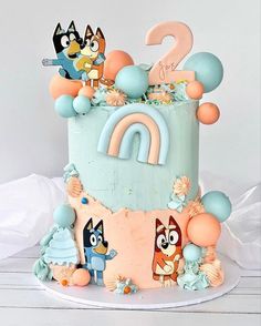 a two tiered cake decorated with cartoon characters and an animal figure on top, sitting on a white table