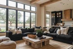 a living room filled with black couches and lots of windows next to a kitchen