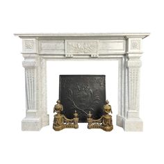 a white fireplace with two golden statues on it's sides and a black plaque in the middle