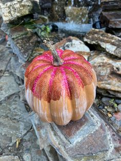 a painted pumpkin sitting on top of a rock next to a water fall with pink sprinkles