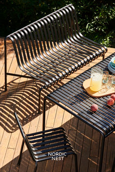 a table with plates and glasses on it next to an iron park bench that is sitting on a wooden deck