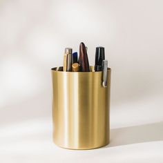 a pen holder with pens and pencils in it on a white surface, against a plain background