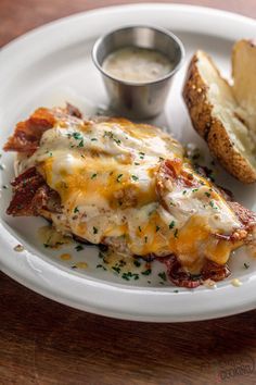 a white plate topped with an enchilada covered in cheese next to bread