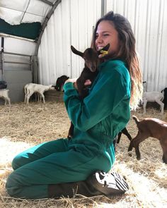 a woman in green jumpsuit holding two baby goats