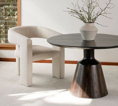 a white vase sitting on top of a wooden table next to a chair and window