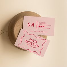 two pink business cards sitting on top of a wooden bowl next to a small plant