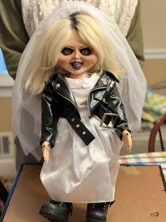 a creepy doll dressed as a bride in a wedding dress and leather jacket on top of a cardboard box