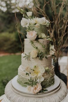 a three tiered cake with flowers and greenery on the top is sitting on a table