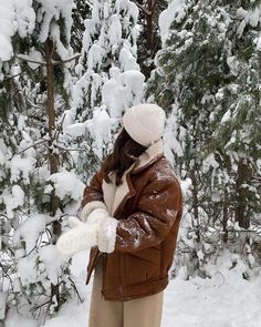 a woman is standing in the snow with her arms out and she has on a brown jacket