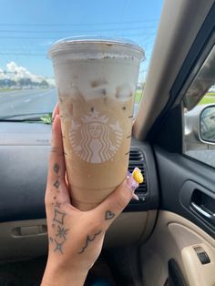 a woman holding up a cup of coffee in her car