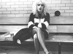 a woman sitting on top of a bench in front of a brick wall with her mouth open