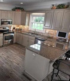 a kitchen with white cabinets and stainless steel appliances, wood flooring and an island in the middle