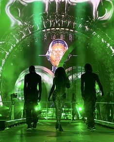 three people walking on stage with green lights behind them and an image of a human head in the background