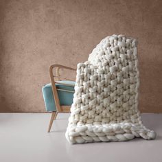 a white blanket sitting on top of a wooden chair next to a blue chair and brown wall