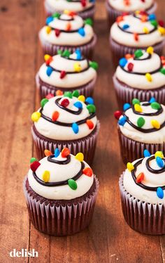 cupcakes decorated with white frosting and multi colored sprinkles on a wooden table