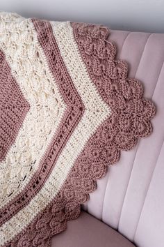 a crocheted blanket sitting on top of a pink couch next to a pillow