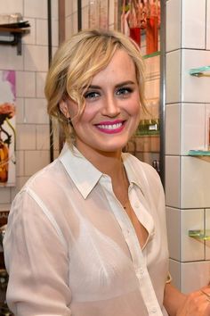 a woman standing in front of a white tiled wall with shelves on either side and she is smiling at the camera