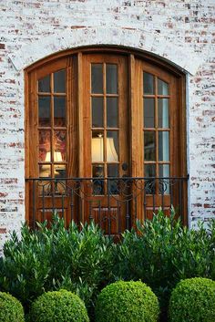 a brick building with two wooden windows and green bushes in front of the window,