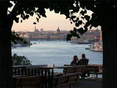 two people are sitting on a bench overlooking the water