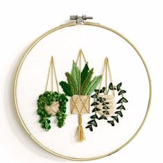 an embroidery project with green plants and leaves on white fabric, hanging from gold hoop