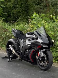 the motorcycle is parked on the side of the road next to some bushes and trees