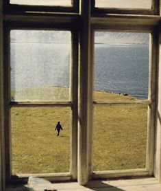 an open window with a person walking in the grass outside and water out side it