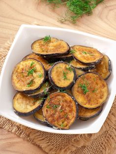 cooked eggplant slices in a white dish on a wooden table with sprigs of green