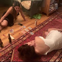 two women are laying on the floor with beer bottles and cards scattered all over them