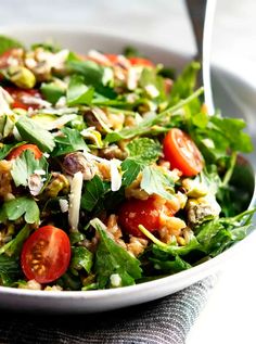 a salad with tomatoes, lettuce and other toppings in a white bowl