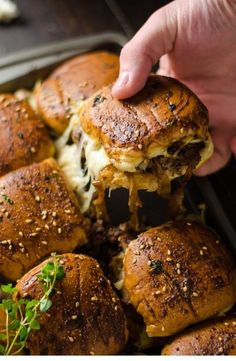 someone is picking up some sliders out of the pan with cheese and herbs on them