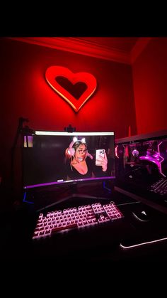 a desktop computer sitting on top of a desk next to a keyboard and monitor in front of a heart shaped neon sign