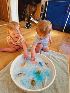 two toddlers playing in a bathtub full of soapy water on the floor