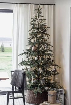 a small christmas tree in a living room next to a window with white drapes