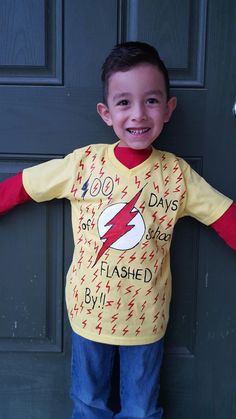 a young boy standing in front of a door wearing a shirt with the flash on it