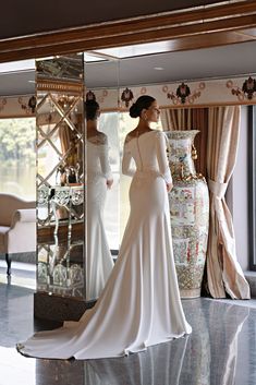 a woman standing in front of a mirror wearing a white dress and looking at herself in the mirror