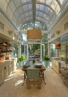 a large kitchen with an arched ceiling and glass windows on the walls, along with a dining table surrounded by potted plants