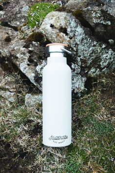 a white water bottle sitting on top of grass next to a large rock and stone wall