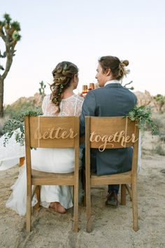 two people sitting on wooden chairs in the sand with their backs turned to each other