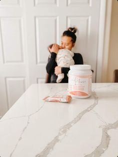 a woman holding a baby in her arms while sitting at a table with some products on it