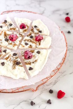 a dessert with white chocolate, raspberries and nuts on a pink plate sitting on a marble table