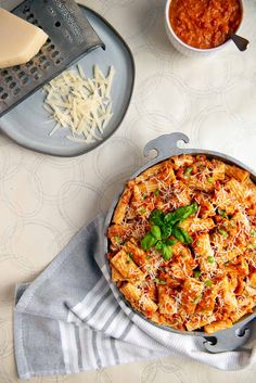 a pasta dish with cheese, sauce and basil on a plate next to a grater