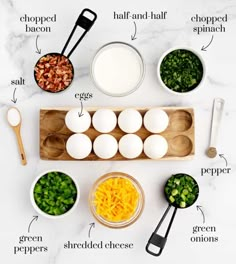 ingredients to make an egg salad laid out on a marble counter top, including hard boiled eggs, shredded cheese, green onions, and chopped bacon