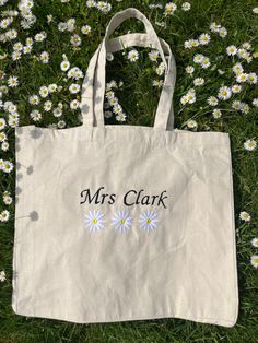 a white tote bag with the words mrs clark on it in front of daisies