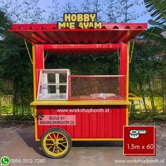 a red and yellow food cart sitting on top of a street next to a lush green forest