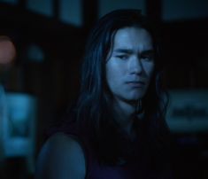 a man with long hair standing in the dark looking at something off to the side